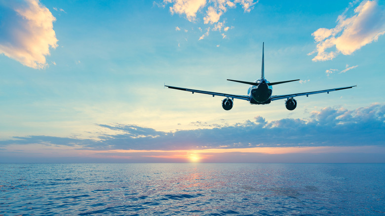 An airliner flies over the ocean toward the setting sun